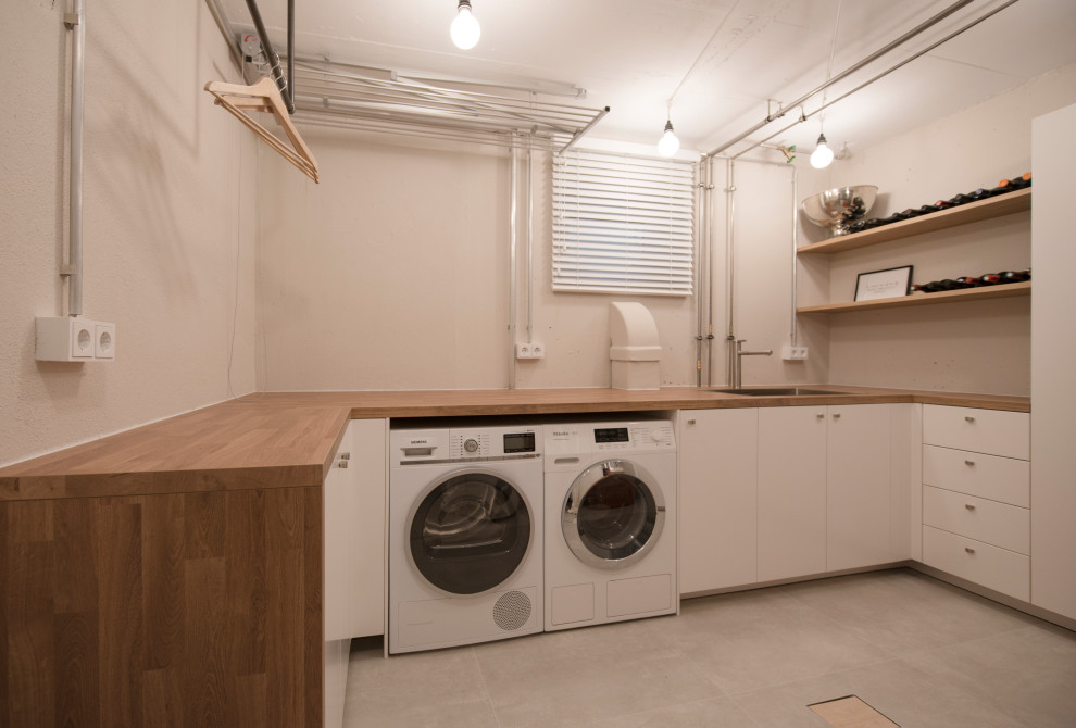 This is an example of a mid-sized u-shaped dedicated laundry room in Munich with a drop-in sink, flat-panel cabinets, white cabinets, laminate benchtops, beige walls, ceramic floors, a side-by-side washer and dryer, grey floor and brown benchtop.