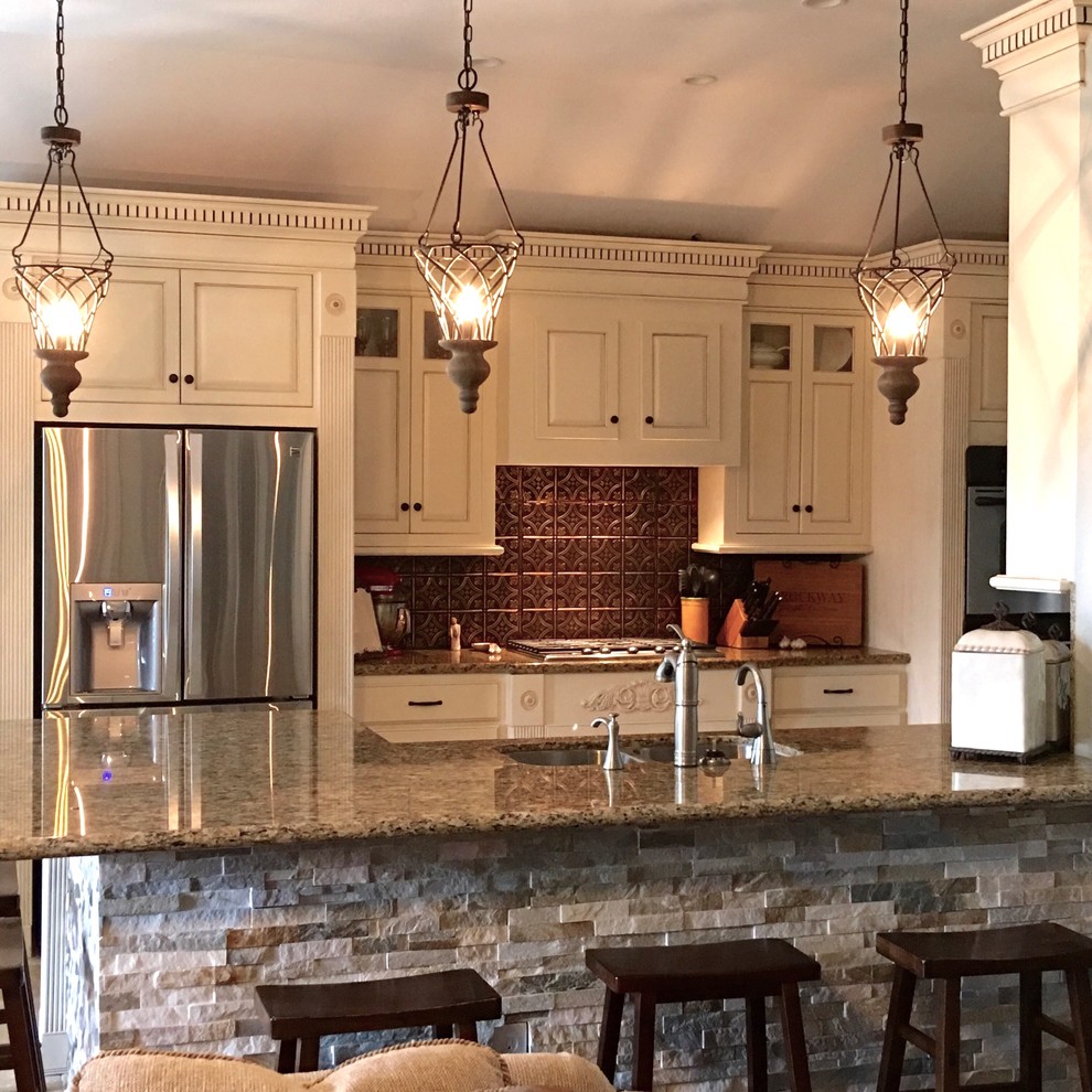 Inspiration for a mid-sized transitional eat-in kitchen in Houston with a drop-in sink, raised-panel cabinets, distressed cabinets, granite benchtops, metallic splashback, stainless steel appliances, limestone floors and a peninsula.