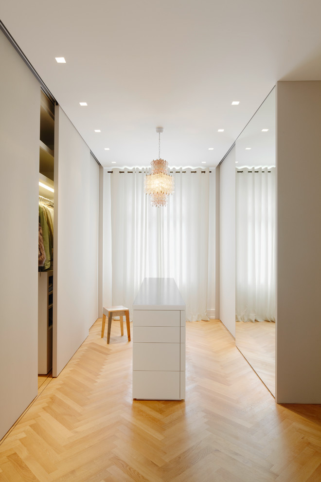This is an example of a large traditional gender-neutral dressing room in Frankfurt with white cabinets and medium hardwood floors.