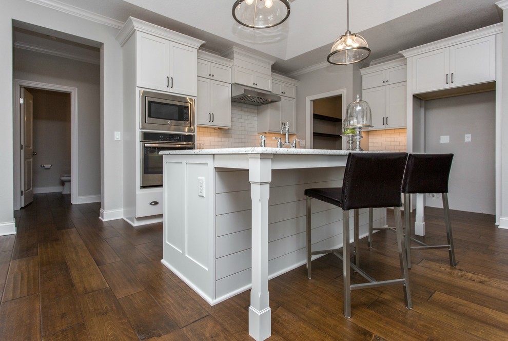 Open concept kitchen - mid-sized transitional single-wall medium tone wood floor and beige floor open concept kitchen idea with a farmhouse sink, recessed-panel cabinets, white cabinets, granite countertops, white backsplash, ceramic backsplash, stainless steel appliances and an island