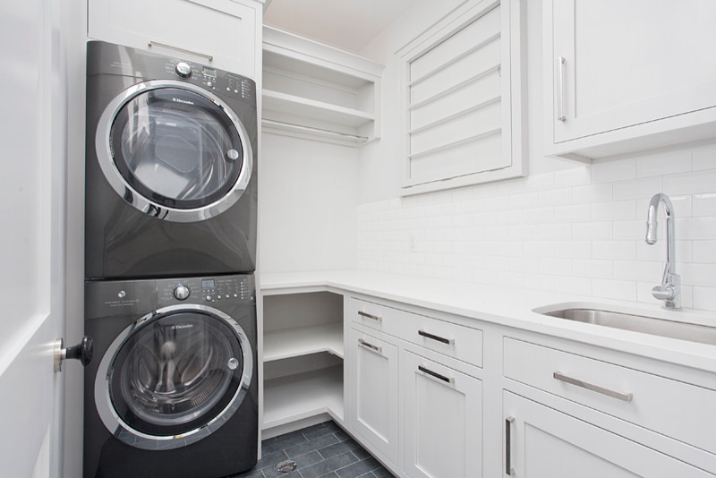 Design ideas for a large transitional l-shaped dedicated laundry room in New York with an undermount sink, shaker cabinets, grey cabinets, quartz benchtops, white walls, travertine floors and a stacked washer and dryer.