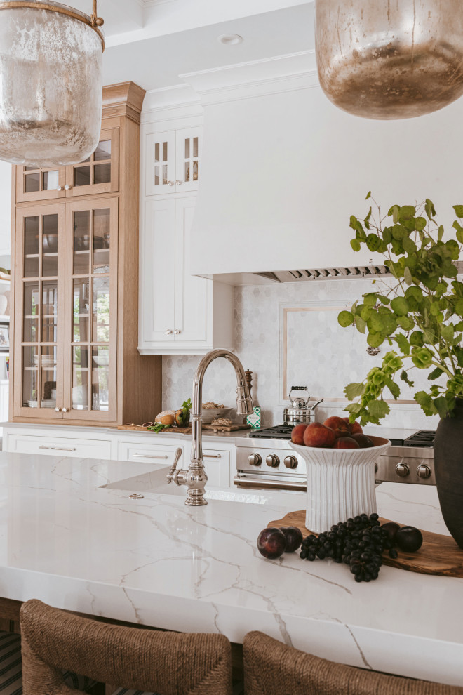 Grand Haven Custom Home - The grand white kitchen is warmed up by select white oak stained island and display cabinet. Quartz cabinets, marble  mosaic backsplash with hints of soft antique brass finishes.
