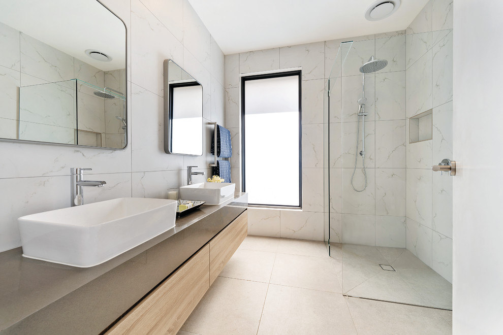 This is an example of a mid-sized contemporary master bathroom in Melbourne with light wood cabinets, a freestanding tub, a corner shower, a one-piece toilet, white tile, ceramic tile, white walls, ceramic floors, engineered quartz benchtops, grey floor, an open shower, grey benchtops and flat-panel cabinets.