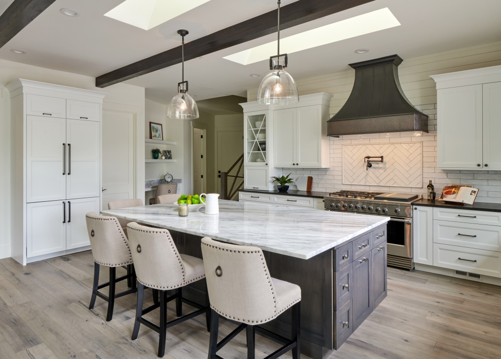 Large cottage u-shaped light wood floor, gray floor and exposed beam open concept kitchen photo in Seattle with a farmhouse sink, recessed-panel cabinets, white cabinets, quartzite countertops, white backsplash, ceramic backsplash, paneled appliances, an island and white countertops