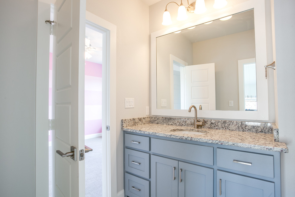 Design ideas for a mid-sized transitional kids bathroom in Dallas with shaker cabinets, blue cabinets, a drop-in tub, a shower/bathtub combo, a one-piece toilet, gray tile, ceramic tile, grey walls, ceramic floors, an undermount sink, granite benchtops, grey floor and a shower curtain.