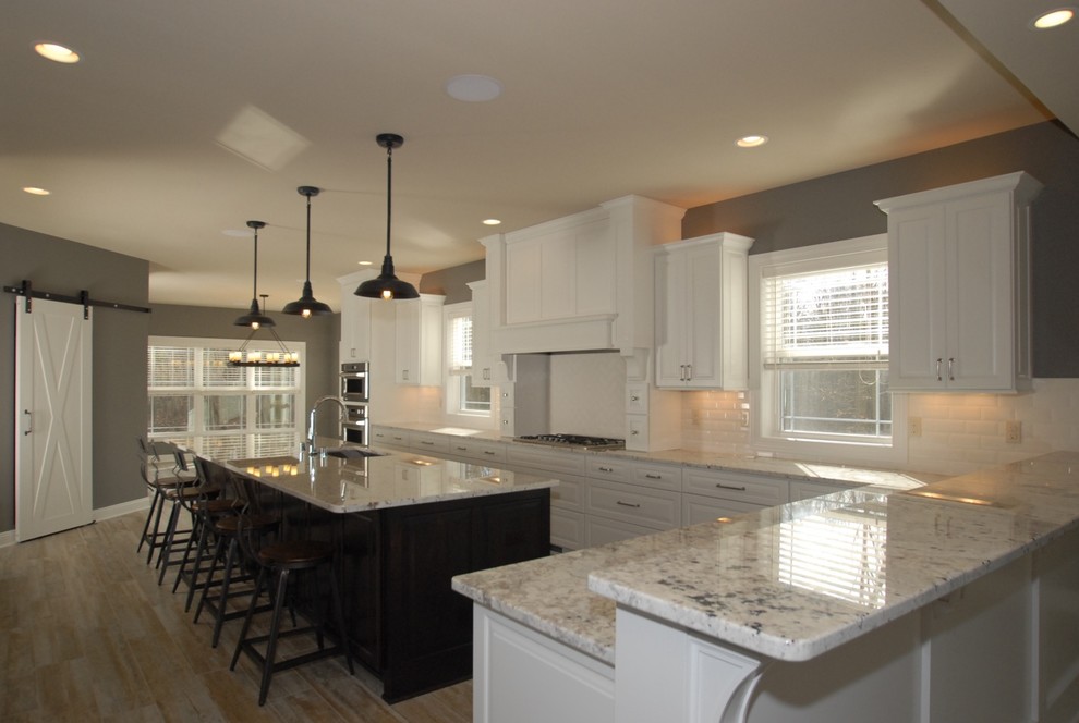 Large transitional galley porcelain tile eat-in kitchen photo in Milwaukee with an undermount sink, raised-panel cabinets, white cabinets, granite countertops, white backsplash, subway tile backsplash, stainless steel appliances and an island