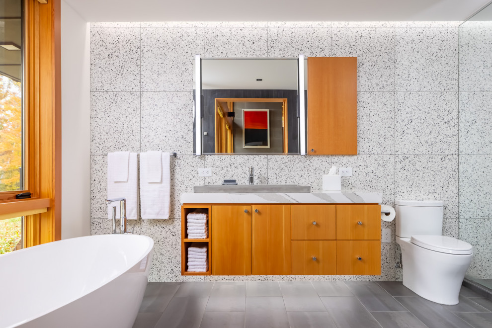 Medium sized rustic ensuite bathroom in Minneapolis with flat-panel cabinets, medium wood cabinets, a freestanding bath, porcelain tiles, white walls, porcelain flooring, engineered stone worktops, grey floors, white worktops, a single sink, a floating vanity unit, grey tiles and a built-in sink.
