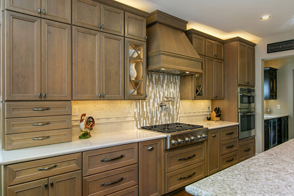Example of a large transitional l-shaped medium tone wood floor and brown floor open concept kitchen design in San Diego with a farmhouse sink, recessed-panel cabinets, medium tone wood cabinets, beige backsplash, paneled appliances, an island, quartz countertops and travertine backsplash