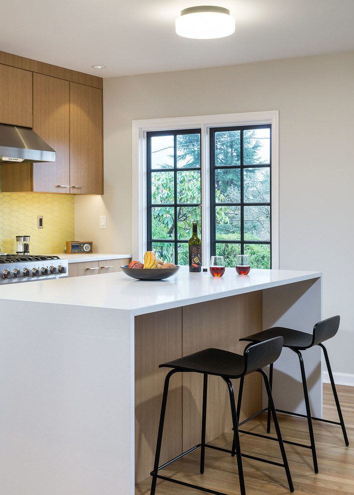 This is an example of a contemporary l-shaped eat-in kitchen in Portland with flat-panel cabinets, medium wood cabinets, quartz benchtops, yellow splashback, ceramic splashback, stainless steel appliances, medium hardwood floors and with island.