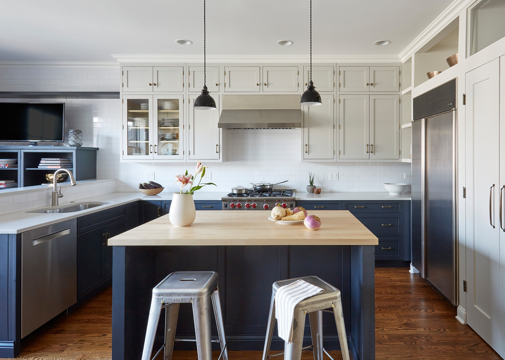 Example of a transitional u-shaped dark wood floor and brown floor kitchen design in Chicago with an undermount sink, shaker cabinets, blue cabinets, white backsplash, subway tile backsplash, stainless steel appliances and an island