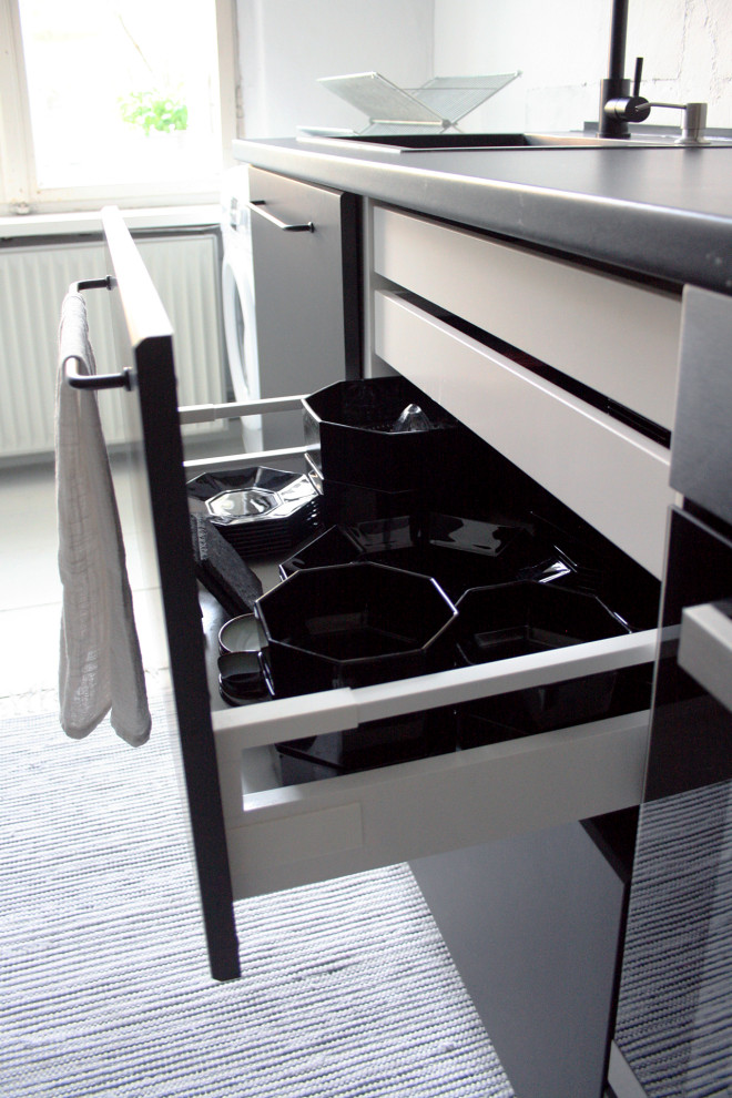 Industriell inredning av ett litet svart linjärt svart kök och matrum, med en enkel diskho, släta luckor, svarta skåp, laminatbänkskiva, svarta vitvaror, ljust trägolv och vitt golv