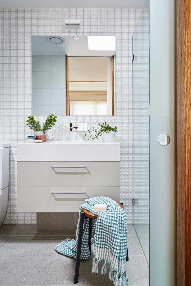 This is an example of a small contemporary 3/4 bathroom in Melbourne with beige cabinets, porcelain tile, white walls, solid surface benchtops, flat-panel cabinets, a curbless shower and an integrated sink.