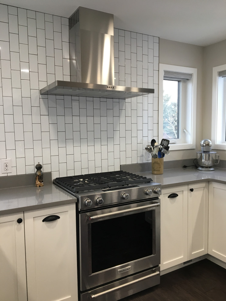 Kitchen - mid-sized transitional u-shaped dark wood floor and brown floor kitchen idea with a farmhouse sink, shaker cabinets, white cabinets, quartzite countertops, white backsplash, subway tile backsplash, stainless steel appliances, an island and gray countertops