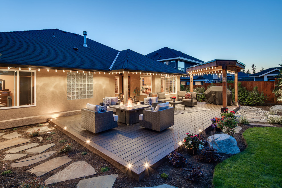 This is an example of a large beach style backyard and ground level deck in Vancouver with a fire feature and an awning.