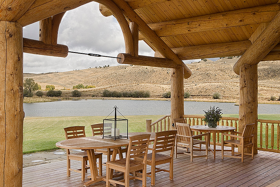 Example of a large mountain style backyard deck design with a roof extension