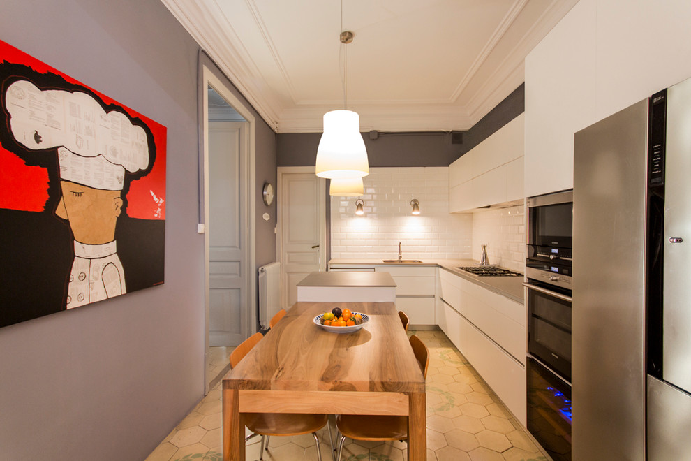 This is an example of a mid-sized contemporary l-shaped separate kitchen in Barcelona with a drop-in sink, flat-panel cabinets, white cabinets, marble benchtops, white splashback, ceramic splashback, stainless steel appliances and with island.