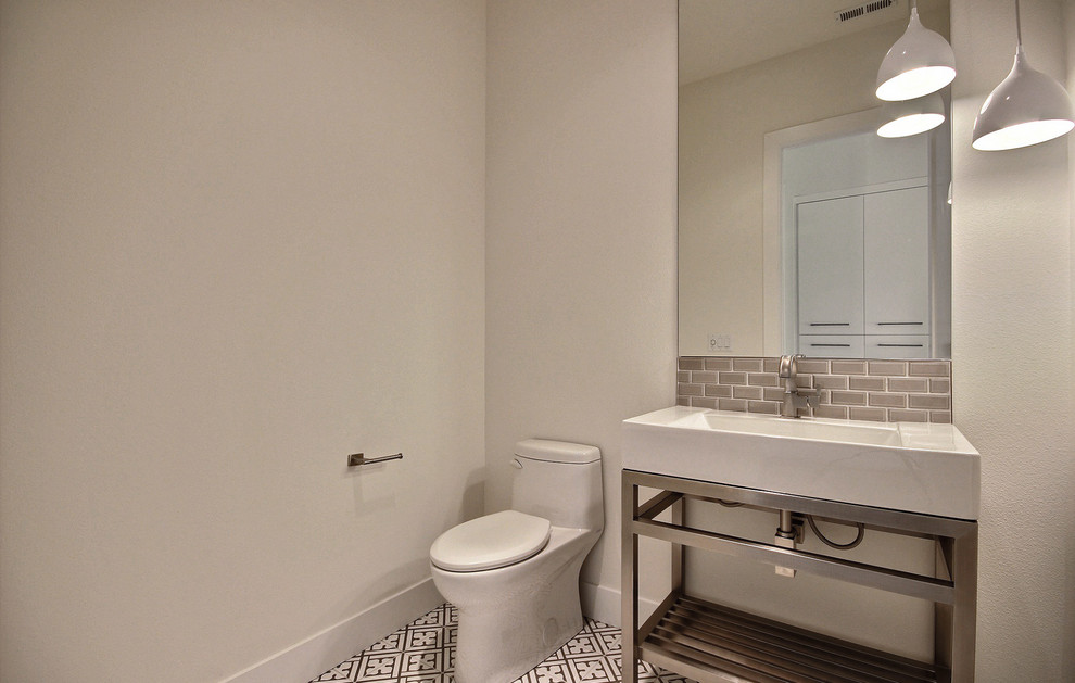 This is an example of a mid-sized modern powder room in Portland with open cabinets, a bidet, gray tile, glass tile, beige walls, ceramic floors, a pedestal sink, multi-coloured floor and white benchtops.