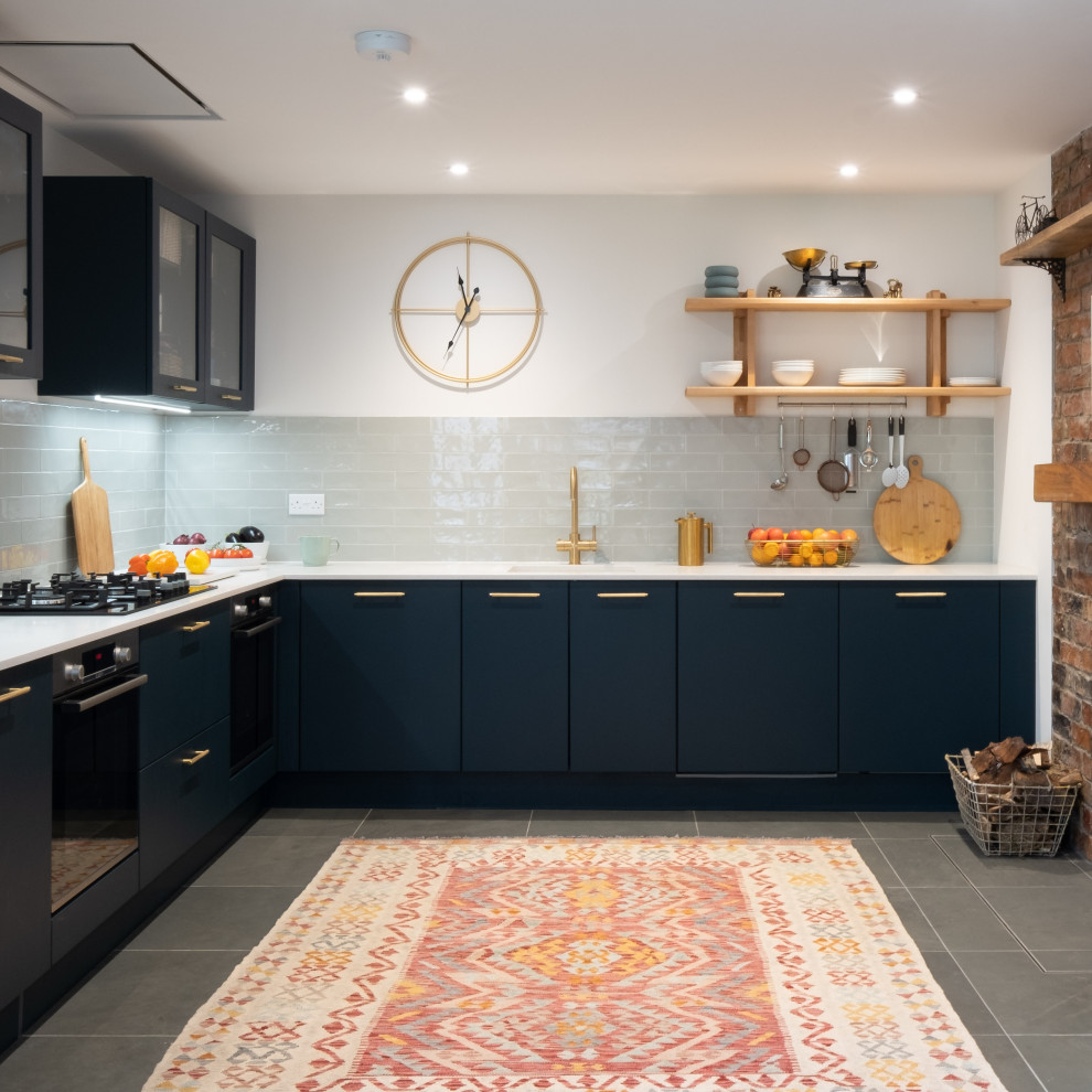 Design ideas for a medium sized bohemian l-shaped open plan kitchen in Gloucestershire with a single-bowl sink, blue cabinets, black appliances, slate flooring, white worktops, flat-panel cabinets, green splashback, porcelain splashback and green floors.