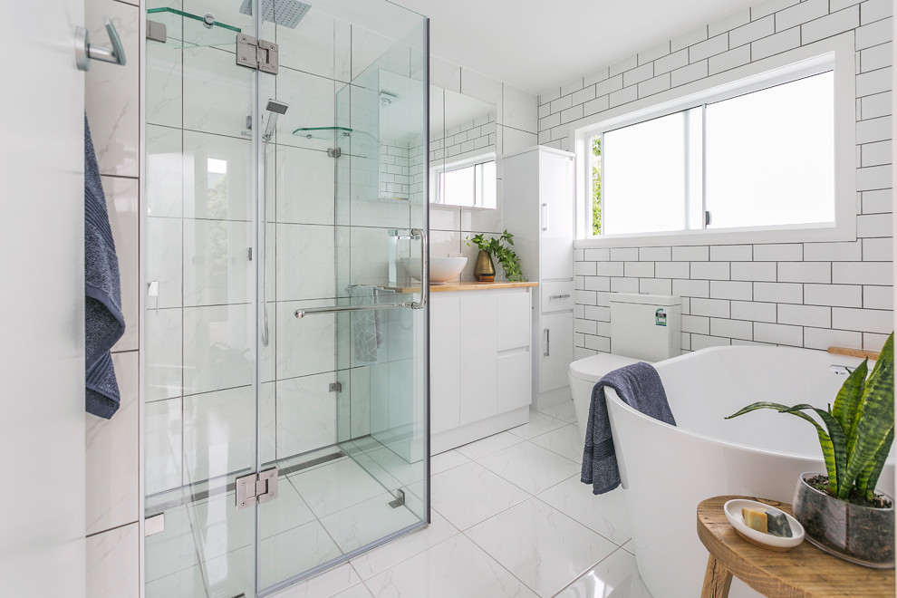 Design ideas for a contemporary master bathroom in Hobart with flat-panel cabinets, white cabinets, a freestanding tub, a corner shower, a two-piece toilet, white tile, white walls, a vessel sink, wood benchtops, white floor and a hinged shower door.