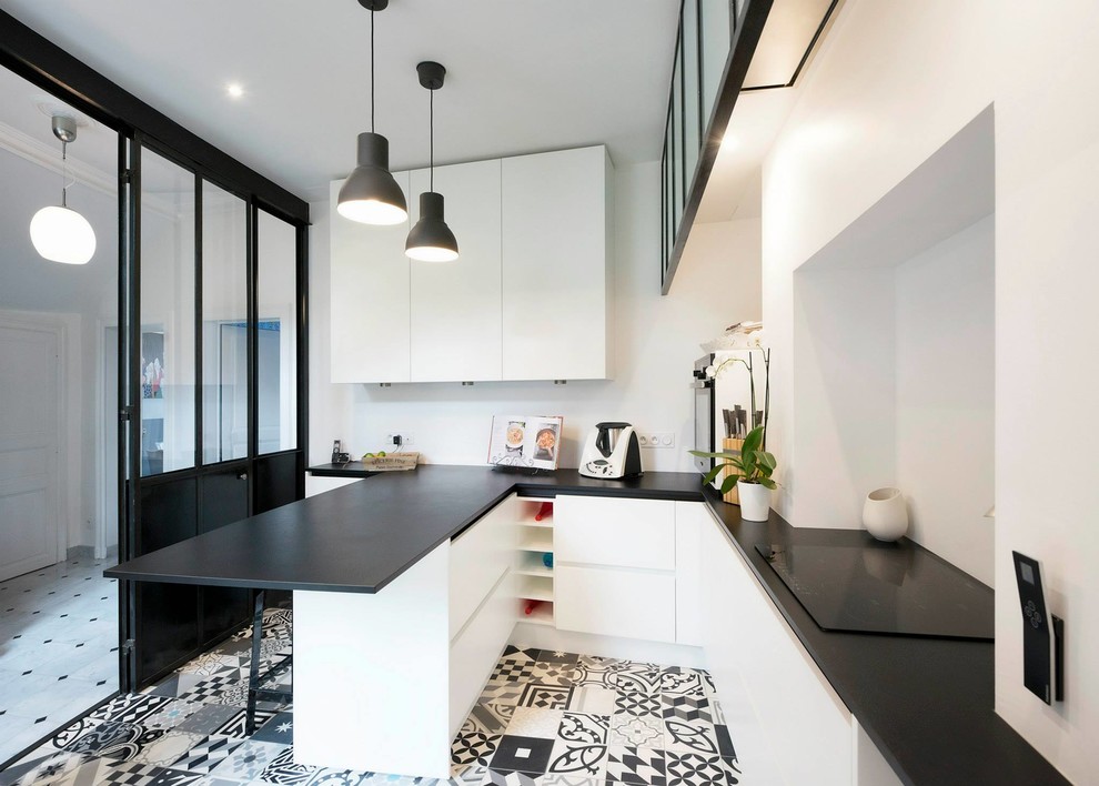 Photo of a mid-sized contemporary u-shaped eat-in kitchen in Paris with a peninsula, an undermount sink, solid surface benchtops, white splashback, ceramic splashback, cement tiles, white floor and black benchtop.