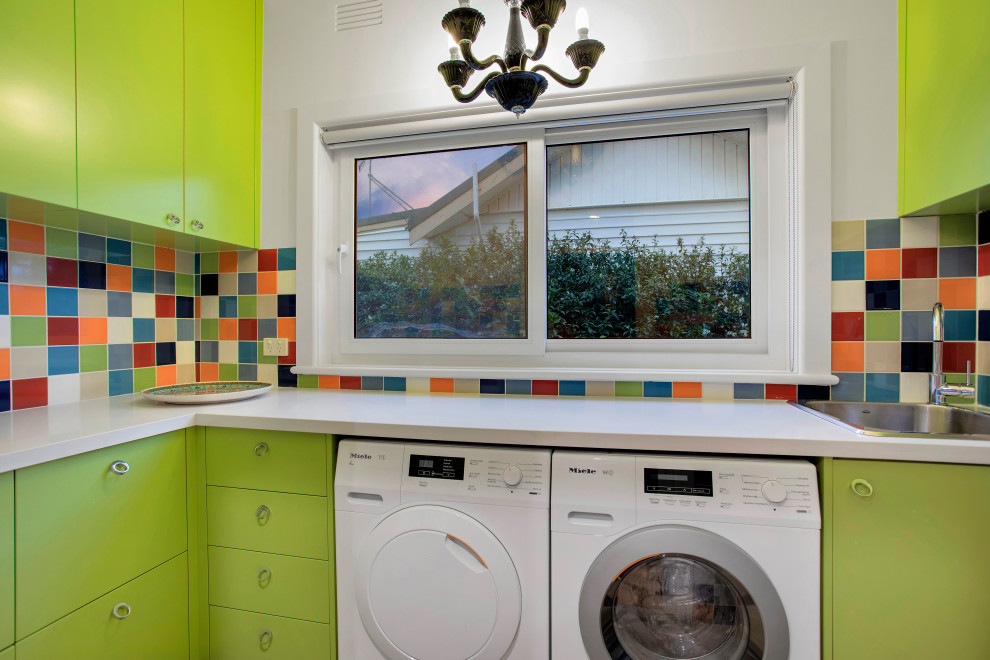 Inspiration for a large eclectic l-shaped dedicated laundry room in Melbourne with a single-bowl sink, flat-panel cabinets, green cabinets, quartz benchtops, multi-coloured splashback, ceramic splashback, white walls, porcelain floors, a side-by-side washer and dryer, beige floor and white benchtop.