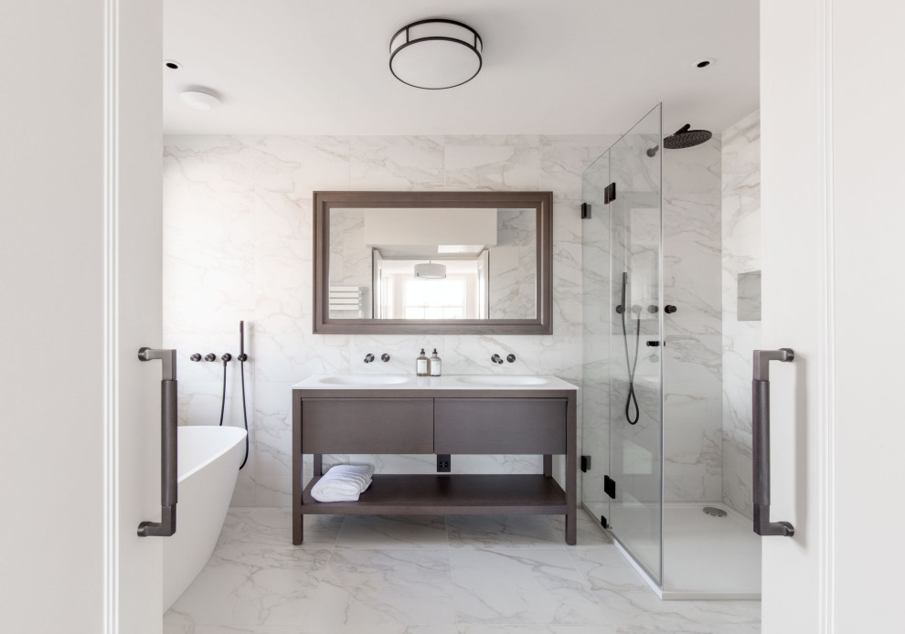 Photo of a classic bathroom in Hertfordshire with flat-panel cabinets, dark wood cabinets, a freestanding bath, a corner shower, white tiles, an integrated sink, grey floors, a hinged door, white worktops, double sinks and a freestanding vanity unit.