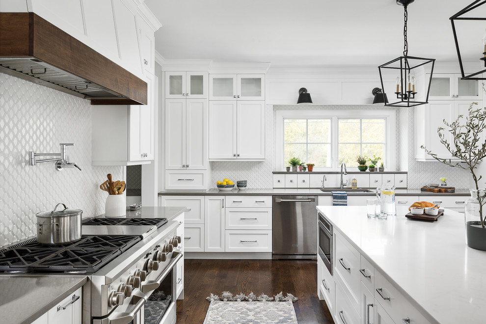 Photo of a large beach style eat-in kitchen in Chicago with an undermount sink, beaded inset cabinets, white cabinets, quartz benchtops, white splashback, ceramic splashback, stainless steel appliances, medium hardwood floors, with island, brown floor and white benchtop.