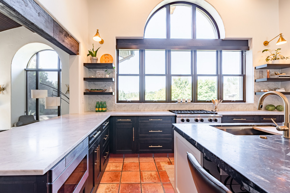 Inspiration for an expansive eclectic eat-in kitchen in Denver with an undermount sink, recessed-panel cabinets, distressed cabinets, granite benchtops, stainless steel appliances, terra-cotta floors, with island, red floor, multi-coloured benchtop and exposed beam.