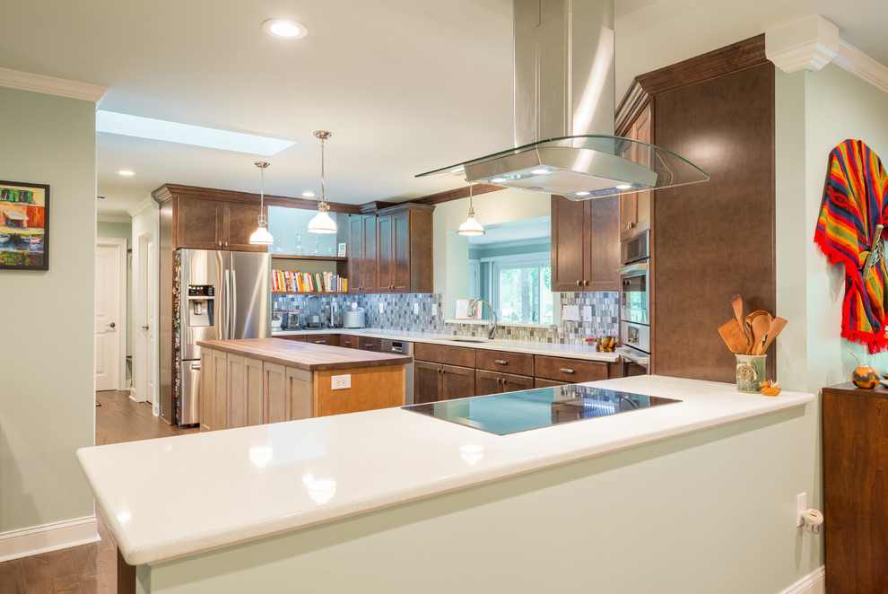 Inspiration for a mid-sized dark wood floor eat-in kitchen remodel with shaker cabinets, brown cabinets, glass tile backsplash, stainless steel appliances and an island