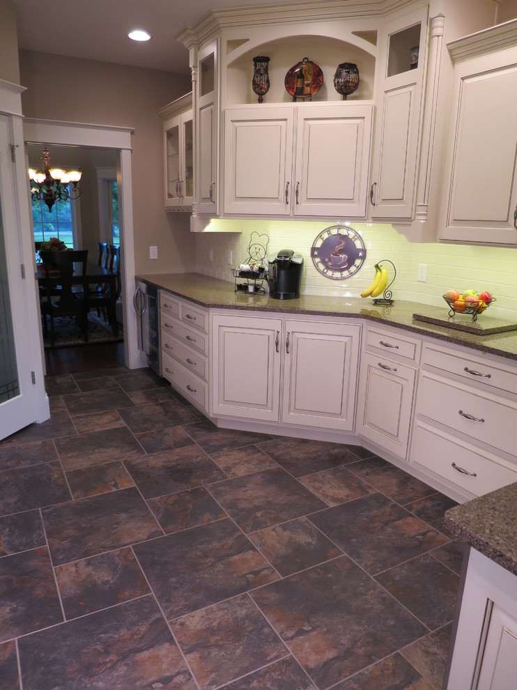 Eat-in kitchen - large transitional galley porcelain tile eat-in kitchen idea with raised-panel cabinets, distressed cabinets, quartz countertops, white backsplash, ceramic backsplash, stainless steel appliances and a peninsula