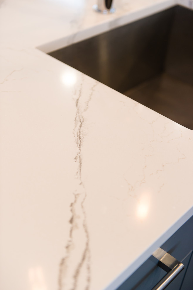 Large trendy l-shaped porcelain tile and gray floor enclosed kitchen photo with an undermount sink, flat-panel cabinets, gray cabinets, quartz countertops, stainless steel appliances, a peninsula and white countertops