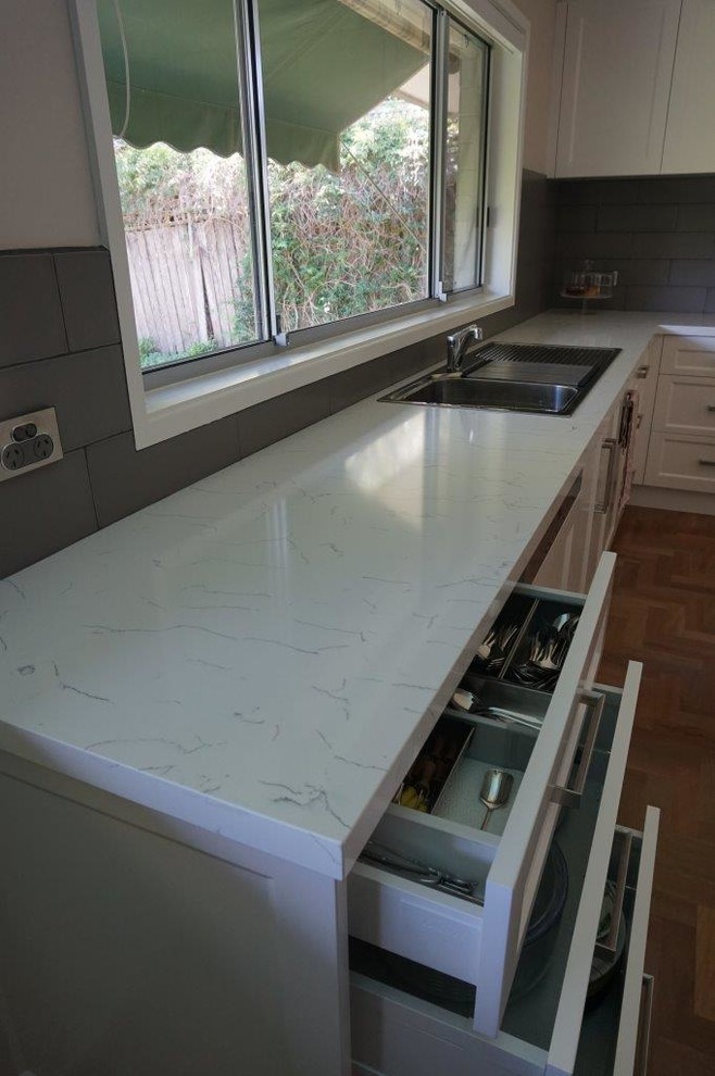 Large contemporary u-shaped kitchen in Sydney with a drop-in sink, shaker cabinets, white cabinets, quartz benchtops, grey splashback, subway tile splashback, stainless steel appliances, medium hardwood floors and with island.