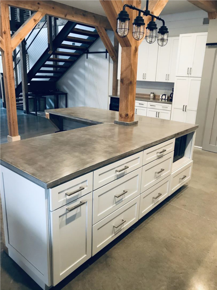 Photo of an expansive country l-shaped eat-in kitchen in Chicago with a farmhouse sink, shaker cabinets, white cabinets, concrete benchtops, timber splashback, black appliances, concrete floors, with island, grey floor, grey benchtop and exposed beam.
