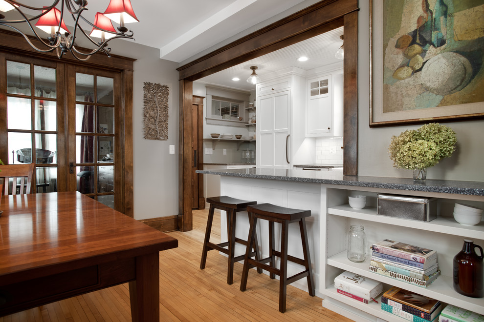 Design ideas for a mid-sized traditional u-shaped eat-in kitchen in Minneapolis with a farmhouse sink, shaker cabinets, white cabinets, recycled glass benchtops, white splashback, subway tile splashback, panelled appliances, light hardwood floors, a peninsula, brown floor and grey benchtop.