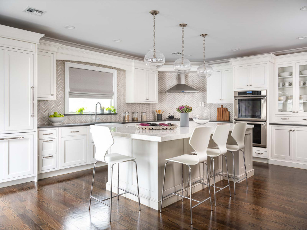 Photo of a large transitional l-shaped kitchen in New York with a farmhouse sink, recessed-panel cabinets, white cabinets, quartz benchtops, beige splashback, porcelain splashback, stainless steel appliances, with island, brown floor, grey benchtop and dark hardwood floors.
