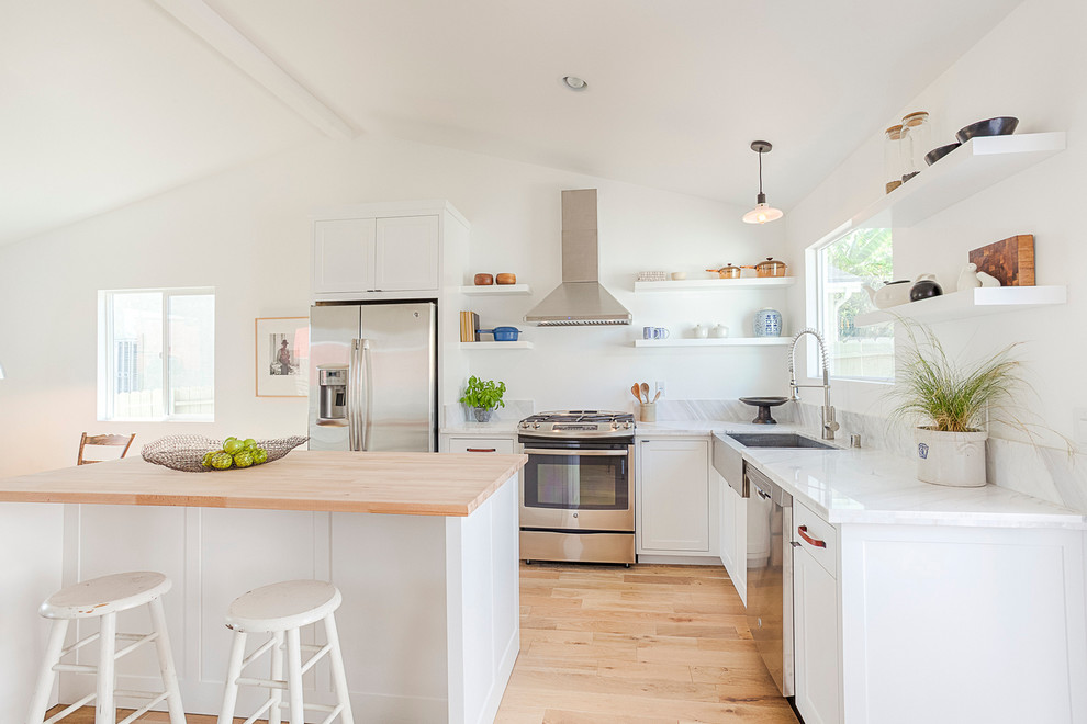 Photo of a contemporary l-shaped kitchen in Other with an undermount sink, shaker cabinets, white cabinets, white splashback, light hardwood floors and with island.