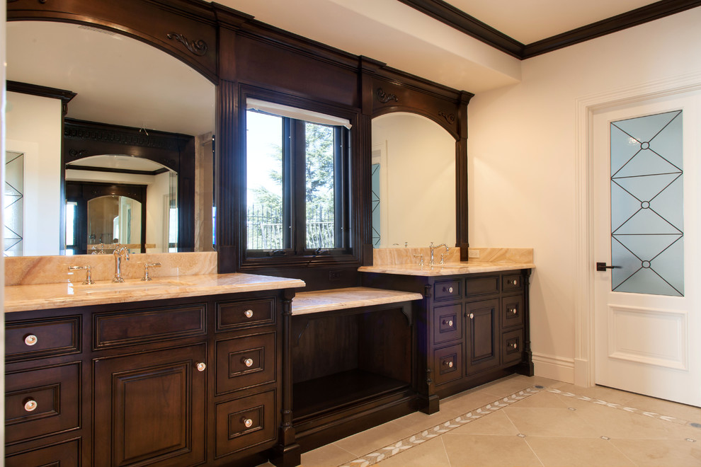 Inspiration for a mid-sized traditional master bathroom in Los Angeles with an undermount sink, raised-panel cabinets, dark wood cabinets, onyx benchtops, a drop-in tub, an alcove shower, a two-piece toilet, beige tile, mosaic tile, white walls and mosaic tile floors.