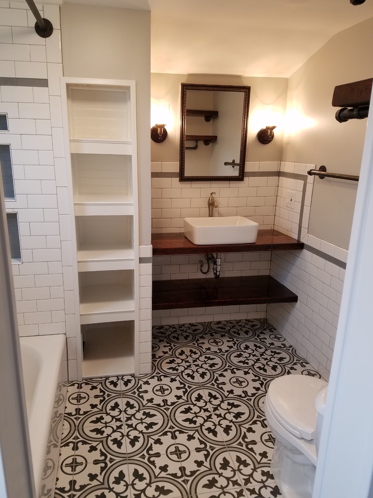 Small country master bathroom in St Louis with distressed cabinets, an alcove tub, a shower/bathtub combo, a two-piece toilet, black and white tile, ceramic tile, grey walls, ceramic floors, a vessel sink, wood benchtops, black floor, a shower curtain and brown benchtops.