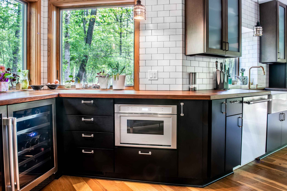 Inspiration for a mid-sized industrial galley eat-in kitchen in Other with a farmhouse sink, flat-panel cabinets, dark wood cabinets, wood benchtops, white splashback, porcelain splashback, stainless steel appliances, medium hardwood floors, with island, brown floor and brown benchtop.