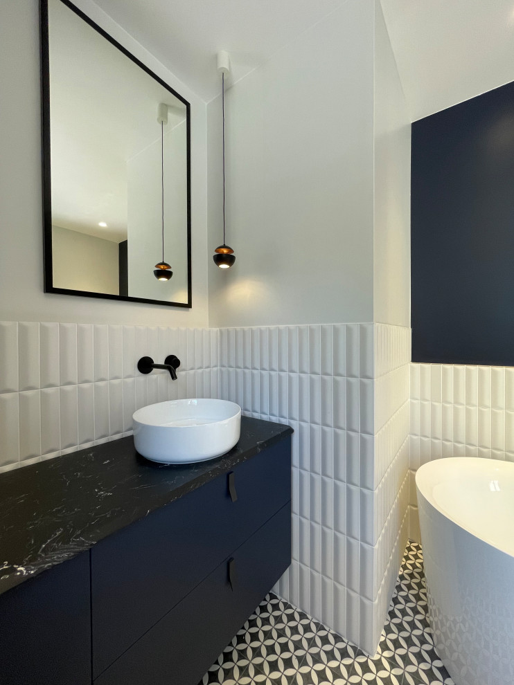 Свежая идея для дизайна: большая главная ванная комната в восточном стиле с синими фасадами, ванной в нише, инсталляцией, белой плиткой, удлиненной плиткой, белыми стенами, полом из цементной плитки, консольной раковиной, мраморной столешницей, открытым душем, черной столешницей, тумбой под одну раковину и подвесной тумбой - отличное фото интерьера