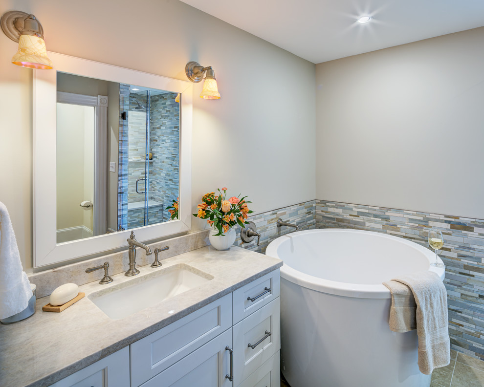Photo of a large transitional master bathroom in DC Metro with shaker cabinets, white cabinets, a japanese tub, an alcove shower, a two-piece toilet, multi-coloured tile, mosaic tile, white walls, travertine floors, an integrated sink, solid surface benchtops, beige floor, a hinged shower door and white benchtops.