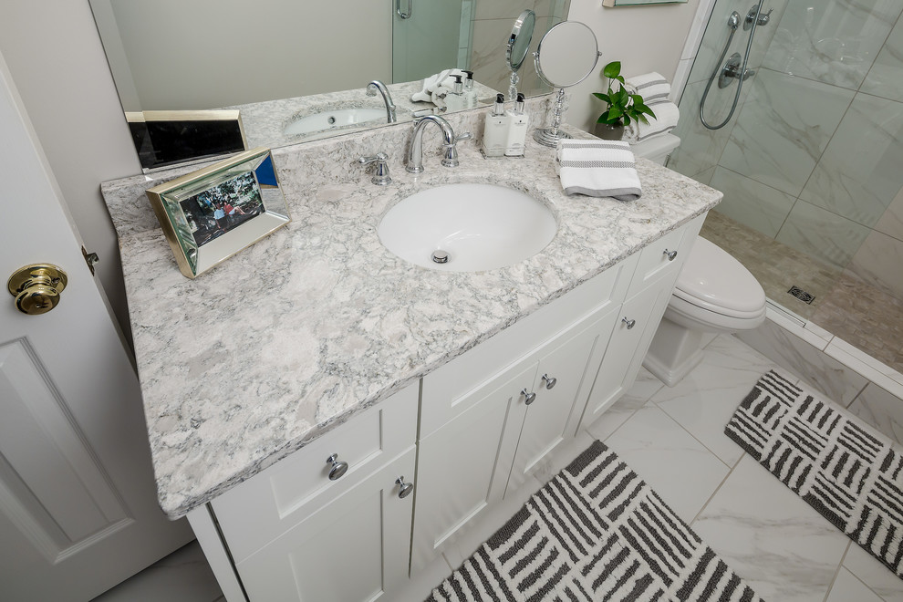 This is an example of a mid-sized transitional master bathroom in Atlanta with shaker cabinets, white cabinets, an open shower, a two-piece toilet, white tile, porcelain tile, grey walls, porcelain floors, an undermount sink and engineered quartz benchtops.