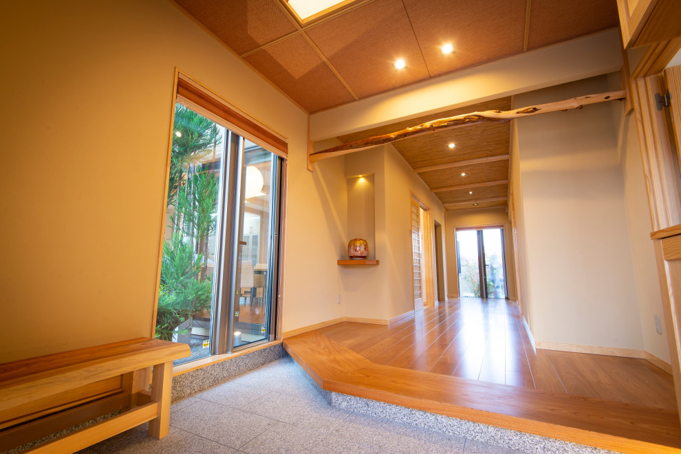 Großer Asiatischer Eingang mit Korridor, beiger Wandfarbe, Granitboden, Schiebetür, hellbrauner Holzhaustür und weißem Boden in Sonstige