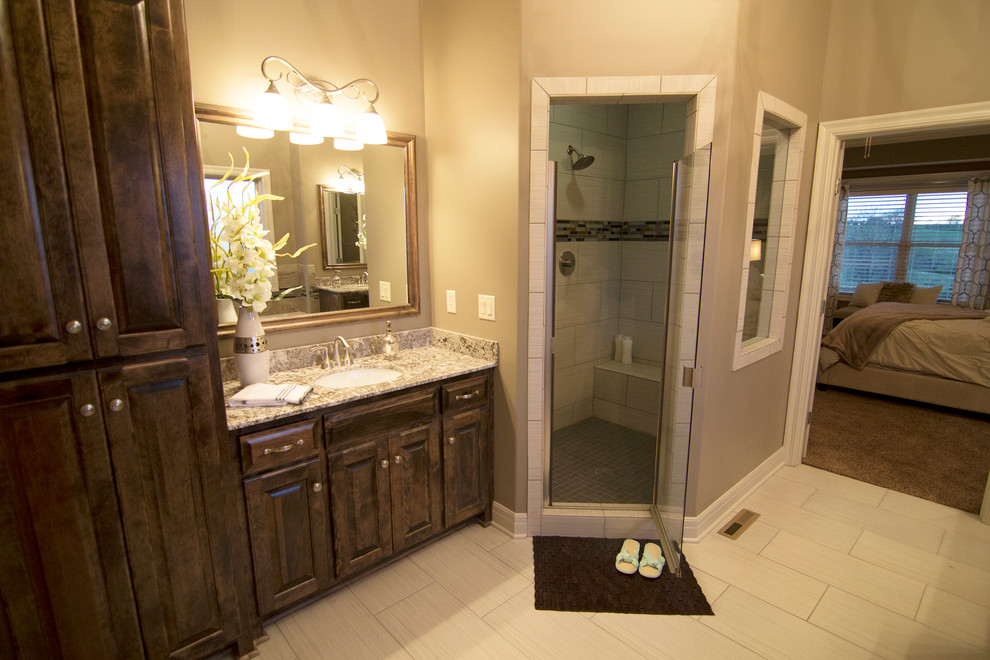 This is an example of a traditional master bathroom in Kansas City with an undermount sink, dark wood cabinets, marble benchtops, white tile, ceramic tile, ceramic floors, raised-panel cabinets, beige walls, an alcove shower and a hinged shower door.