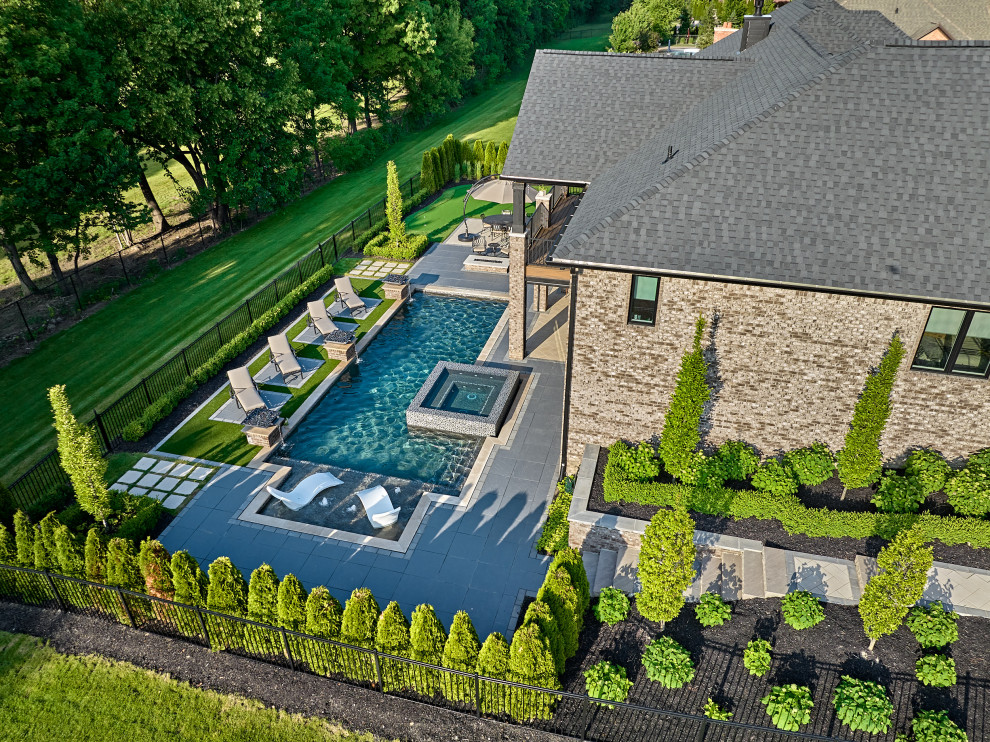 Modelo de piscinas y jacuzzis actuales de tamaño medio a medida en patio trasero con adoquines de hormigón