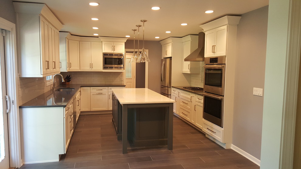 Mid-sized transitional u-shaped eat-in kitchen in Chicago with shaker cabinets, white cabinets, subway tile splashback, stainless steel appliances, with island, quartz benchtops, white splashback, porcelain floors and a single-bowl sink.