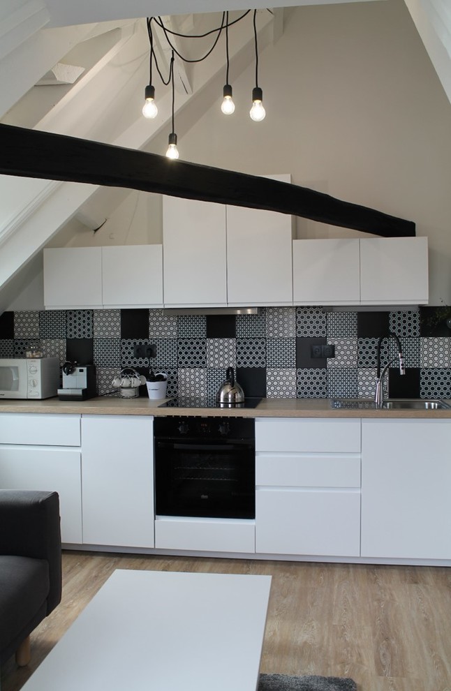 Photo of a mid-sized contemporary single-wall open plan kitchen in Clermont-Ferrand with a drop-in sink, white cabinets, wood benchtops, multi-coloured splashback, cement tile splashback, panelled appliances, light hardwood floors and no island.