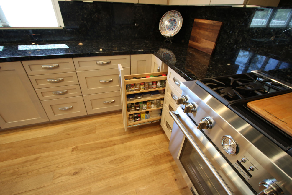 Inspiration for a medium sized classic l-shaped kitchen pantry in Orange County with a belfast sink, shaker cabinets, white cabinets, granite worktops, black splashback, granite splashback, stainless steel appliances, light hardwood flooring, an island, brown floors, multicoloured worktops and a coffered ceiling.