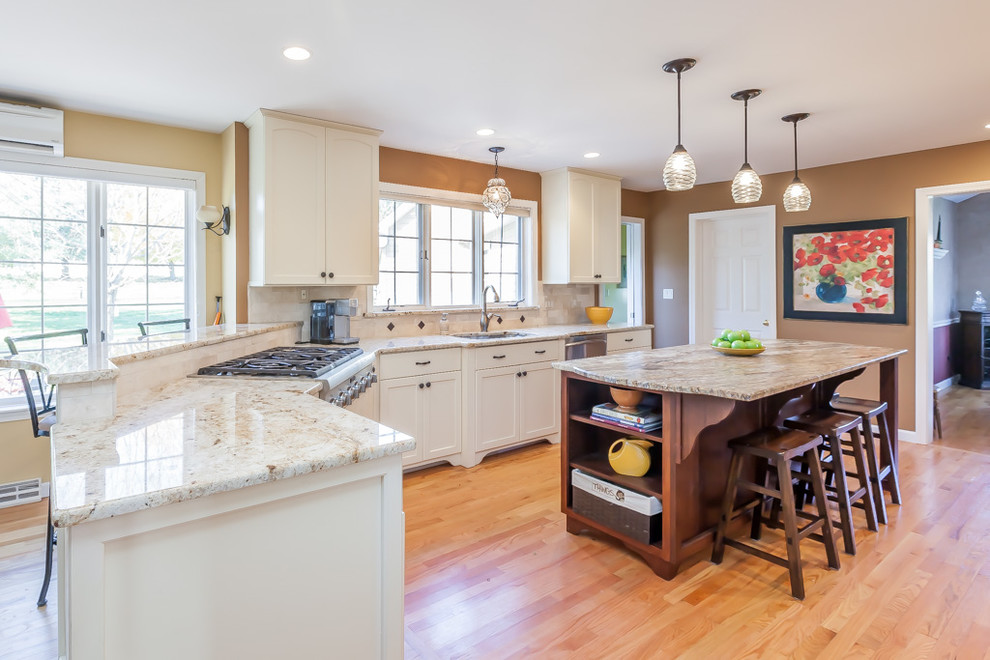 Inspiration for a mid-sized transitional u-shaped light wood floor enclosed kitchen remodel in Boston with a double-bowl sink, recessed-panel cabinets, white cabinets, granite countertops, beige backsplash, stone tile backsplash, stainless steel appliances and an island