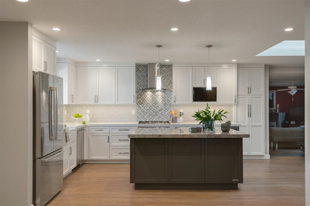 Example of a mid-sized minimalist l-shaped medium tone wood floor and gray floor open concept kitchen design in San Francisco with a farmhouse sink, shaker cabinets, white cabinets, quartz countertops, gray backsplash, ceramic backsplash, stainless steel appliances, an island and gray countertops